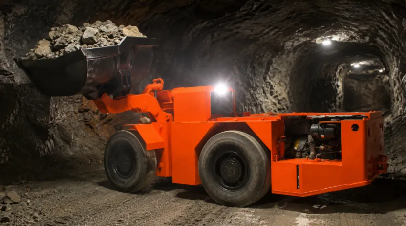 Orange LHD loader carrying rocks in an underground mine tunnel