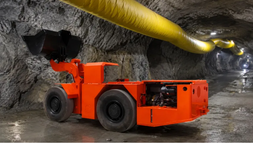 Orange LHD loader under a yellow ventilation duct in a mine