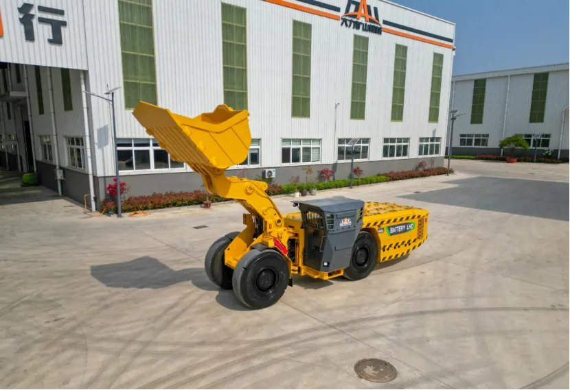 Yellow battery-powered LHD mining loader with a raised bucket parked outside an industrial building