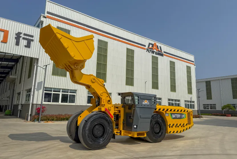 Yellow battery-powered LHD mining loader with raised bucket parked outside a factory