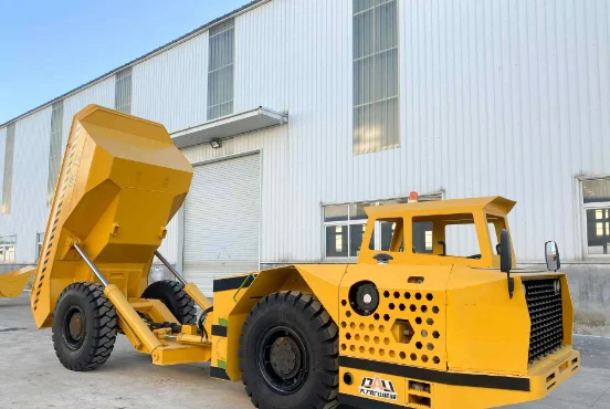 Yellow underground mining dump truck with raised bed parked outside factory